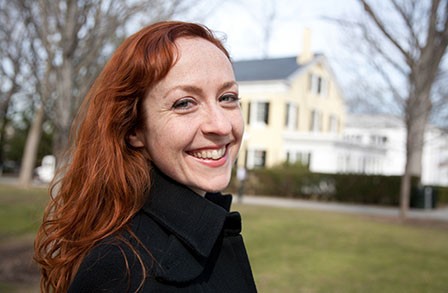 Woman smiling looking at camera with blurry yellow house in background.