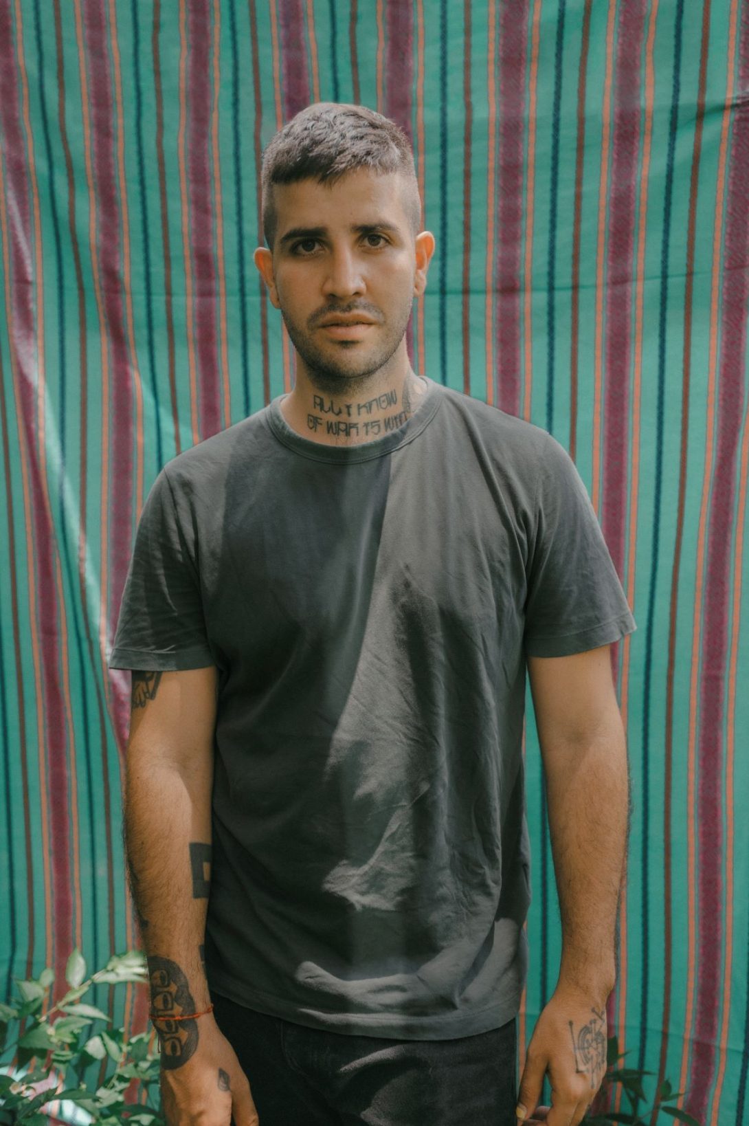 Man with tattoos stands in front of a green and maroon striped background.
