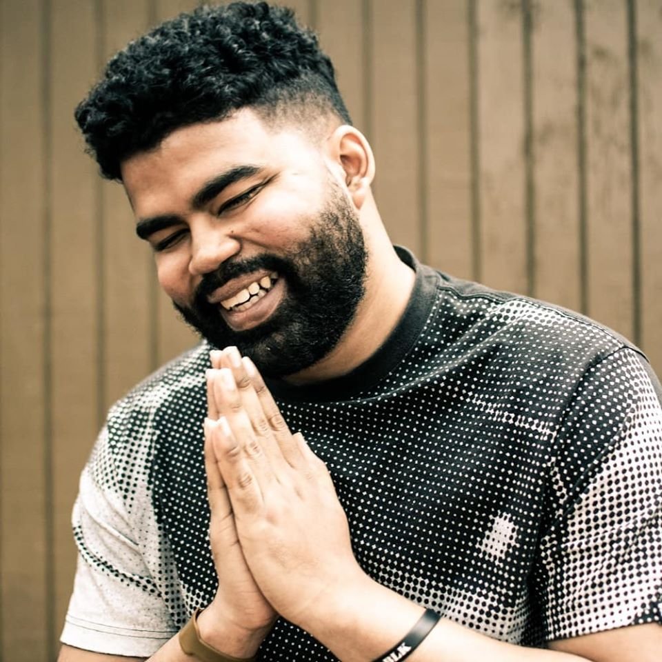 Man smiling with his eyes closed and hands together in prayer pose.